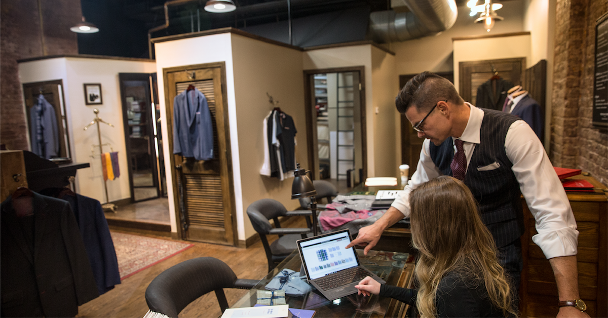 Two retail employees working from a Microsoft laptop in a high-end clothing store.