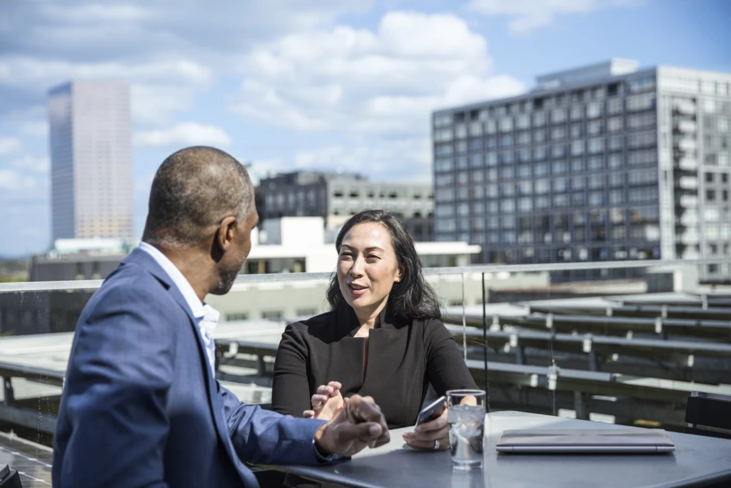 Two business people meeting outside with a city skyline behind them.