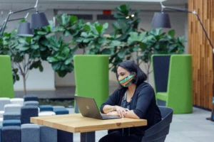 A female employee working on her Surface laptop wearing a mask and smiling.