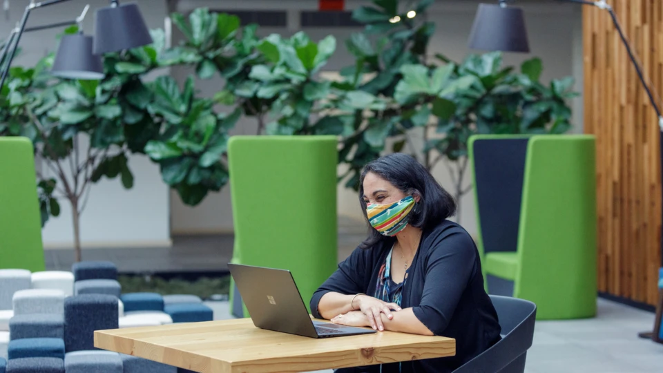 A female employee working on her Surface laptop wearing a mask and smiling.
