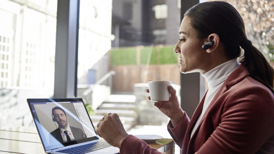 Female small business executive using HP Elite device running Microsoft Teams conference call. Different screens are available: one featuring 1 person on screen, another with 9 people on screen. Keywords: Microsoft Teams, Bluetooth, coffee.