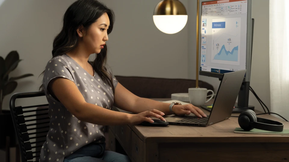 A woman working at her home office on a Lenovo ThinkPad Yoga connected to an external monitor displaying a PowerPoint file. Remote Working collection. Keywords: remote work, remote working, work from home, working at home, home office