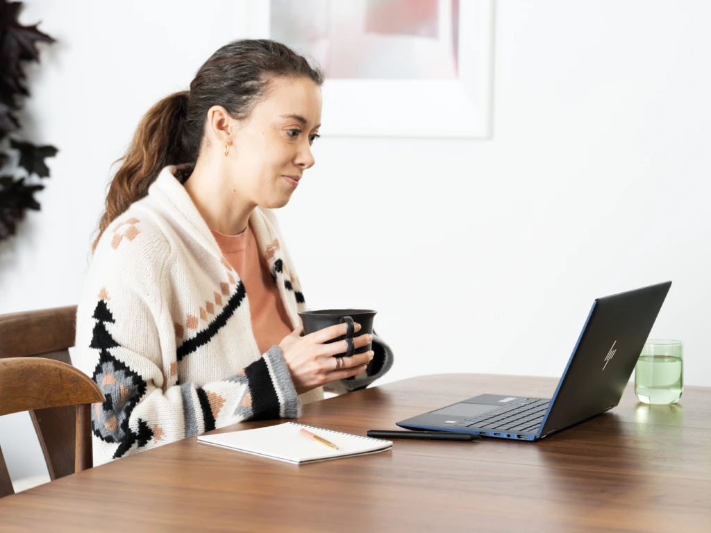 Woman holding a mug with laptop on dining room table with an HP Elite Dragonfly. Keywords: remote work, remote working, work from home, working at home, home office