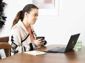Woman holding a mug with laptop on dining room table with an HP Elite Dragonfly. Keywords: remote work, remote working, work from home, working at home, home office