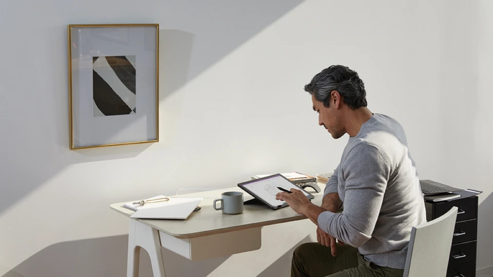 Adult male in home office environment using Microsoft OneNote at a desk with a black Microsoft Surface Pro 7 in studio mode.