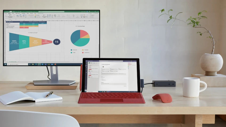 Front view of a Surface Pro 7+ with a poppy red keyboard and poppy red Surface Arc Mouse. Surface Pro 7+ screen is displaying Microsoft Teams and the monitor is displaying Microsoft Excel.