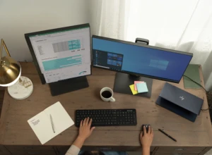 High angle view of a woman (hands only) working from home on her HP Elite Dragonfly configured with a multi-monitor setup displaying Excel, Pwer BI and Windows Start menu. Remote Working collection. Keywords: remote work, remote working, work from home, working at home, home office