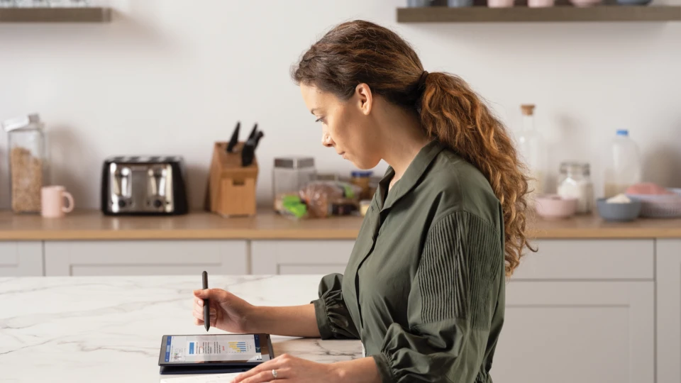 A woman inking a Microsoft Word document displayed on an HP Elite Dragonfly in tablet mode at her kitchen table. Remote Working collection. Keywords: remote work, remote working, work from home, working at home, home office