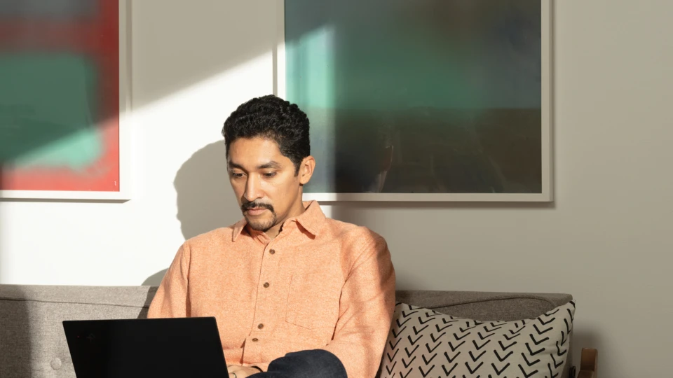 A man sitting on his living room couch working on a Lenovo ThinkPad X1 Carbon. Remote Working collection. Keywords: remote work, remote working, work from home, working at home, home office