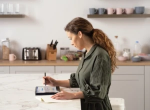 A woman inking a Microsoft Word document displayed on an HP Elite Dragonfly in tablet mode at her kitchen table. Remote Working collection. Keywords: remote work, remote working, work from home, working at home, home office