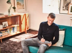 A man sitting on a couch writing in a notebook