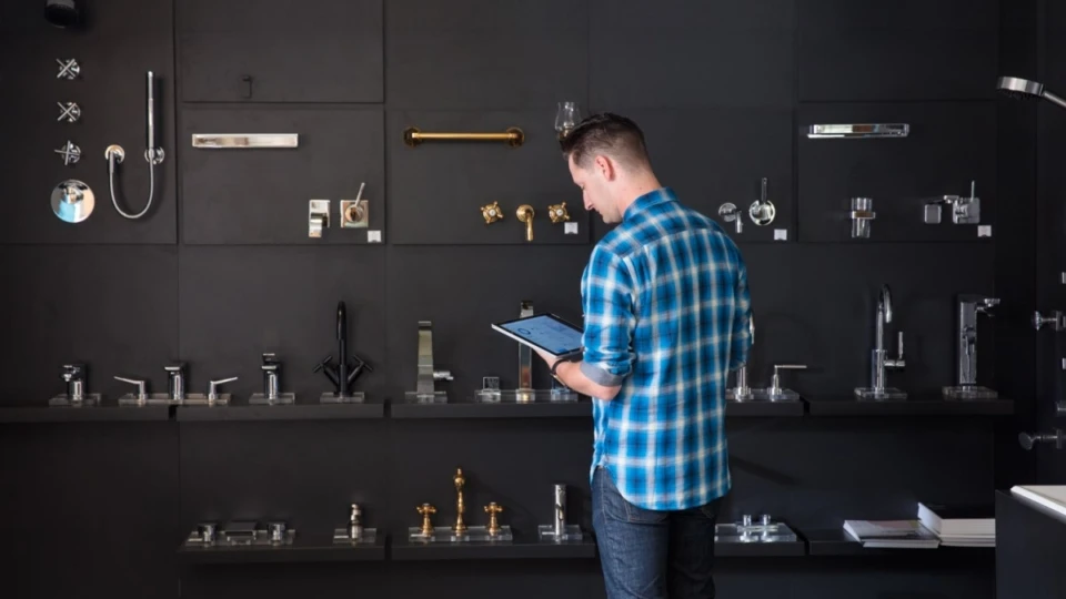 Male millenial using Surface Pro and Surface Pen, standing in front of faucet display wall in a kitchen and bath showroom.