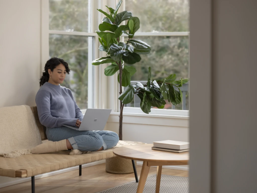 Adult female sitting on couch inside working on Surface Laptop 3
