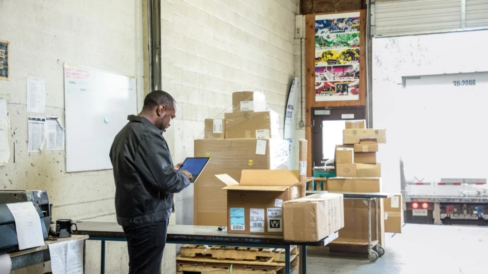 Male employee in warehouse loading dock using Surface Pro. Cardboard packages ready to be loaded on to truck for shipping.