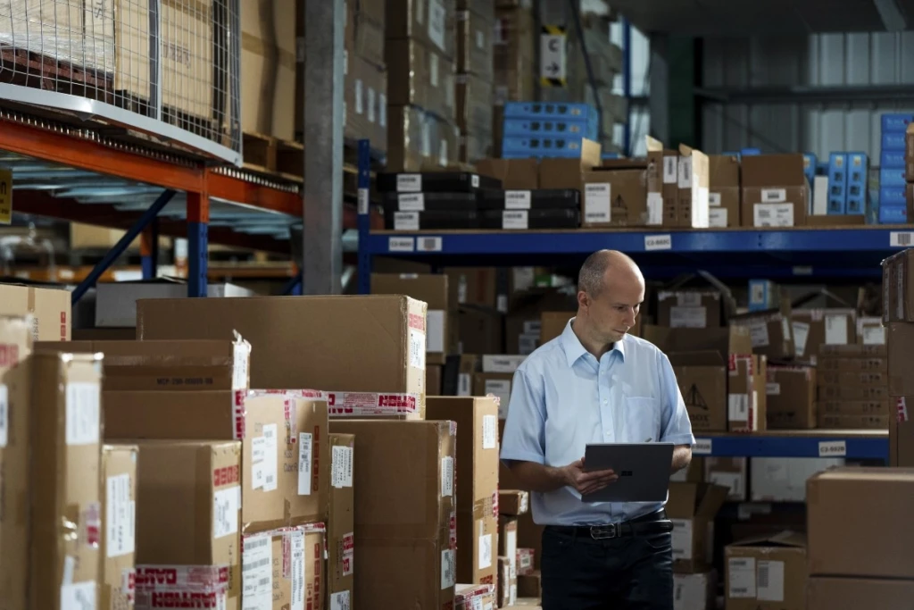 A Firstline Worker in a warehouse using a Surface device as a tablet to make notes. Inventory, Boxes, Supply management, procurement, auditing, review, Business Voice, Microsoft Teams