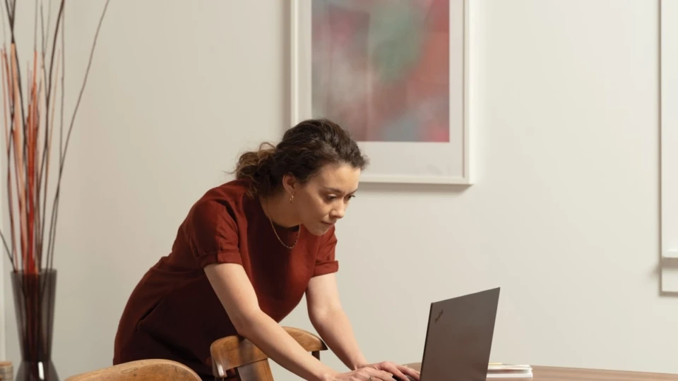 A woman at her diningroom table looking at a Lenovo ThinkPad Yoga. Remote Working collection. Keywords: remote work, remote working, work from home, working at home, home office