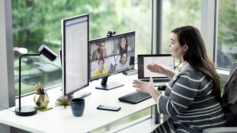 Female enterprise employee working at desk with multiple devices, including HP Elitebook, running a Microsoft Teams conference call. Two different screen images are available: one featuring 4 people on screen, another with 9 people on screen.
