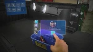 A user’s mixed reality view from their HoloLens, showing their hand using touch controls for starting a holographic video call with a remote colleague.