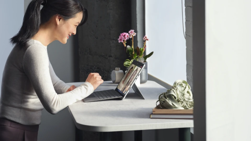 Adult female standing at her desk collaborating via Microsoft Teams video call on a Surface Pro 8 in laptop mode working on a Surface Pro Signature Keyboard.