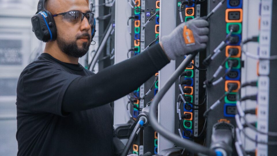 Male datacenter employee plugs cable in hot aisle power distribution unit.