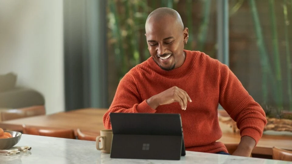 Seller working from home and is on a sales call via Microsoft Teams. Keywords: Dynamics 365; man; hybrid work; business decision maker (BDM); remote work; manager; end user; on the go; Surface tablet; video call