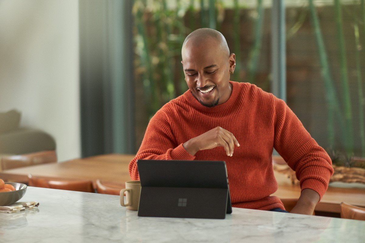 Seller working from home and is on a sales call via Microsoft Teams. Keywords: Dynamics 365; man; hybrid work; business decision maker (BDM); remote work; manager; end user; on the go; Surface tablet; video call