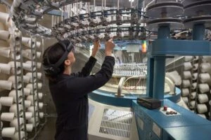 A textile manufacturing factory worker using remote assist on Hololens2 on the warehouse floor. Keywords: One person; on the go; woman; female; operations; training; Dynamics 365; machinery; asset maintenance