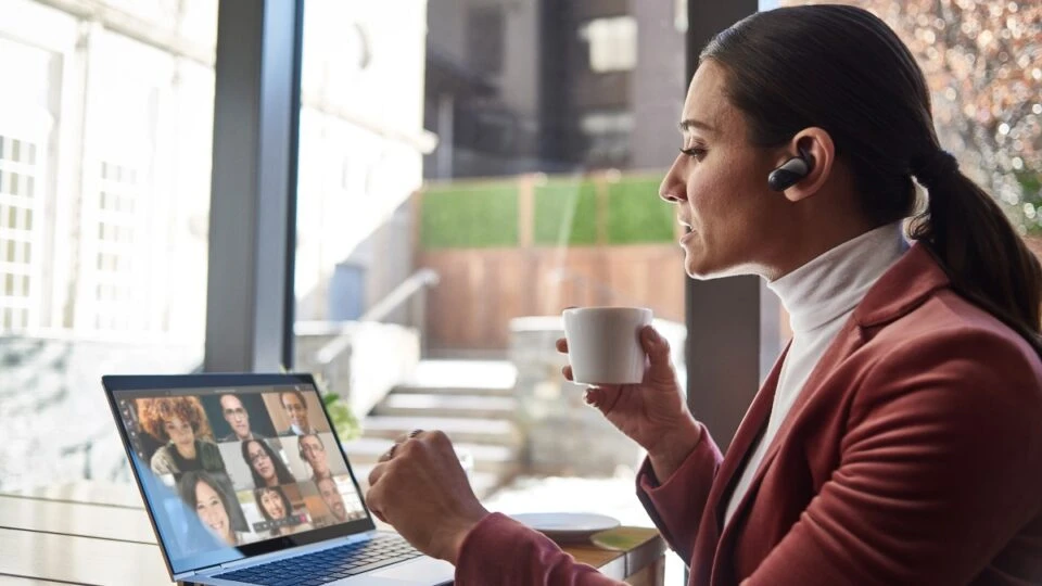 Female small business executive using HP Elite device running Microsoft Teams conference call. Different screens are available: one featuring 1 person on screen, another with 9 people on screen. Keywords: Microsoft Teams, Bluetooth, coffee.