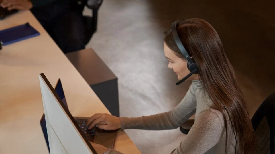 Customer service support call in action. Keywords: Dynamics 365; operations; woman; wearing headset; taking a phone call; typing