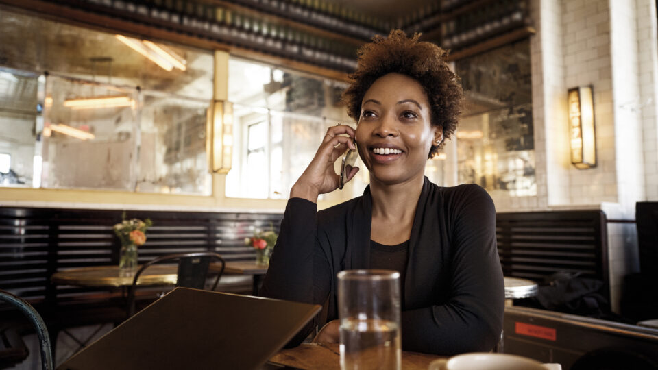 Photo of a young woman smiling while talking on the phone in a cafe.
