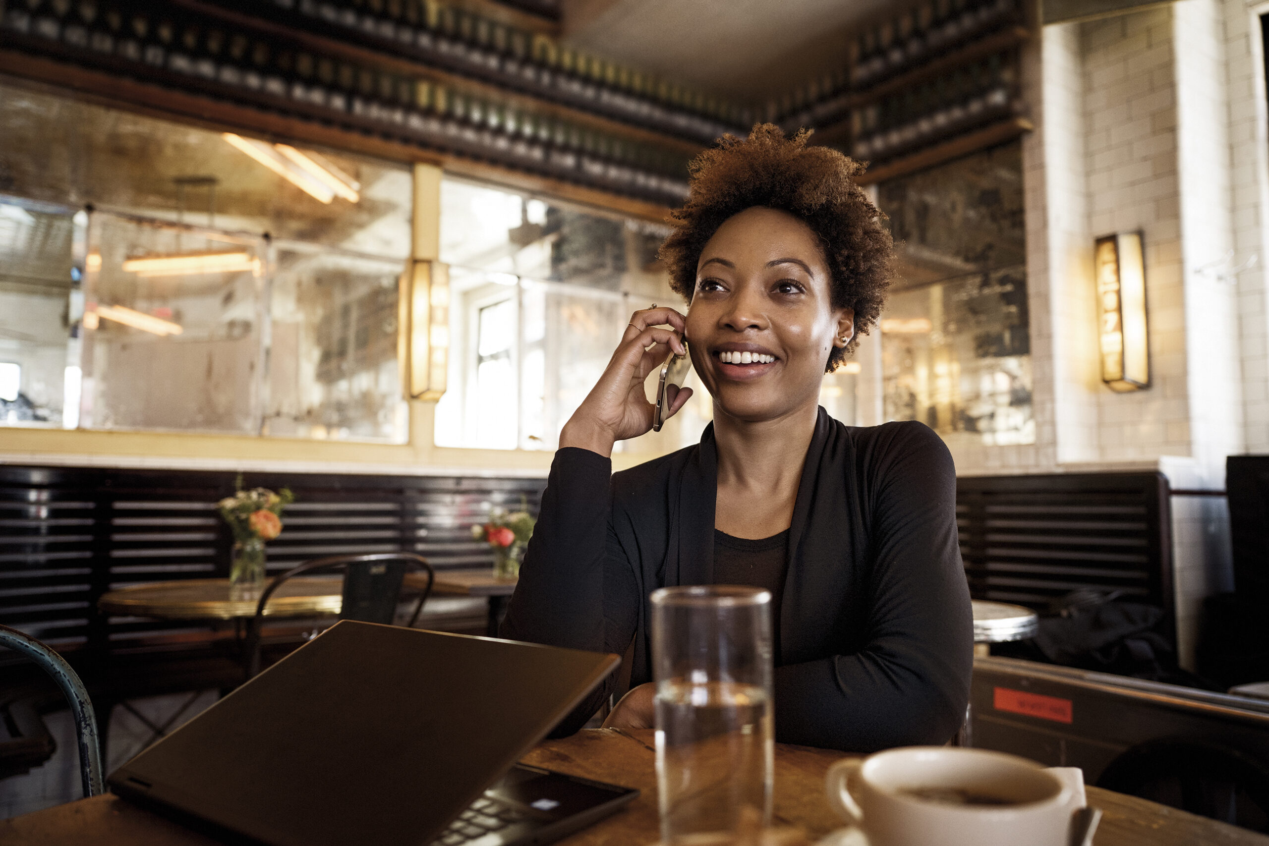 Photo of a young woman smiling while talking on the phone in a cafe.