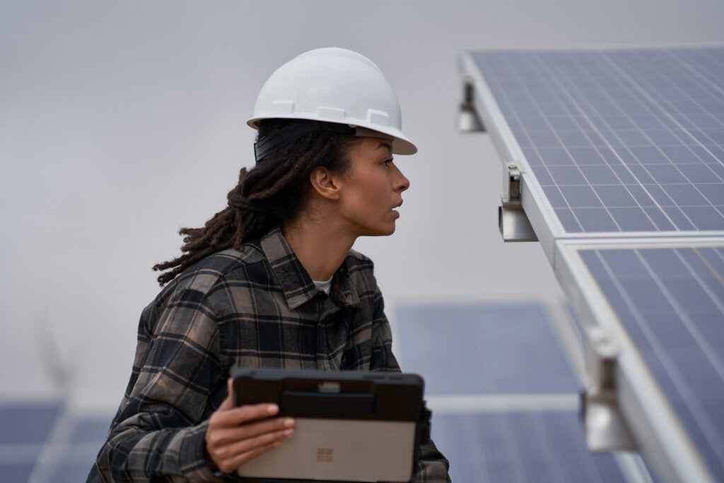 Photo of a female field engineer using a self-service bot to get help inspecting solar panels on a wind farm.