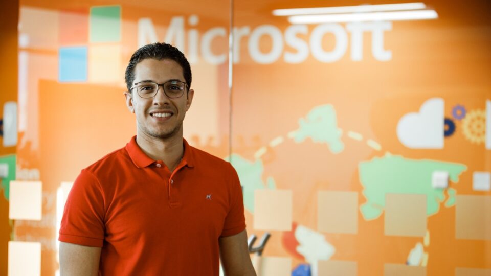 Close up portrait of male office worker standing in front of Microsoft wall display, smiling and looking directly at camera.
