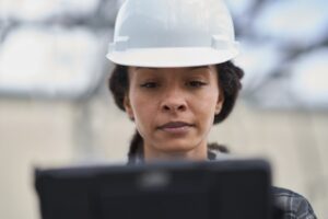 Field engineer wearing hard hat looking at laptop screen.