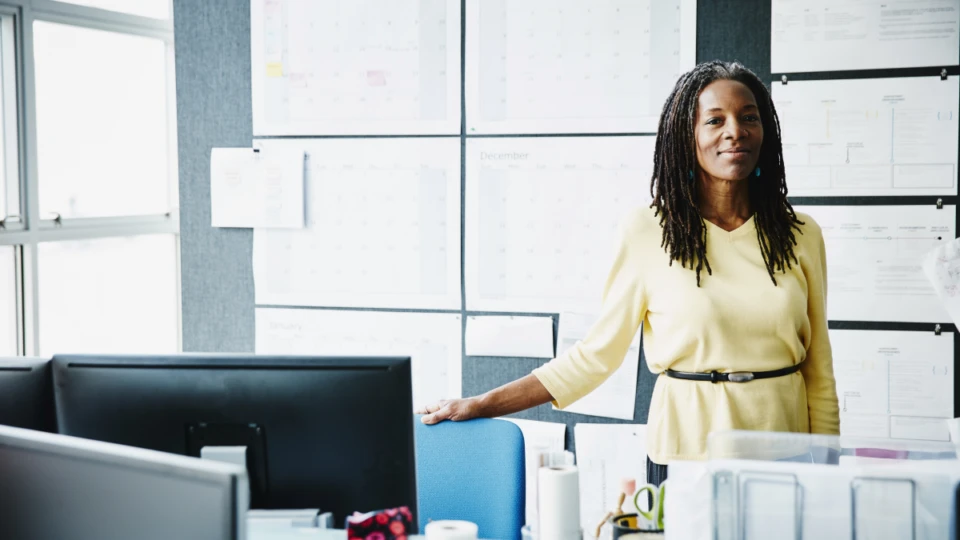 Smiling mature businesswoman standing at workstation in office.