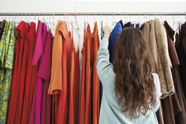 Photo of a woman browsing a rack of clothing in a retail store.