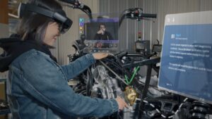 A technician works on a machine using HoloLens to follow instructions and to conduct an inspection meeting with a live video feed showing a remote inspector approving the work.