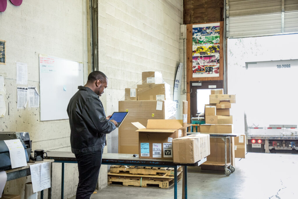 Male warehouse worker at loading dock using Dynamics 365 app on tablet.