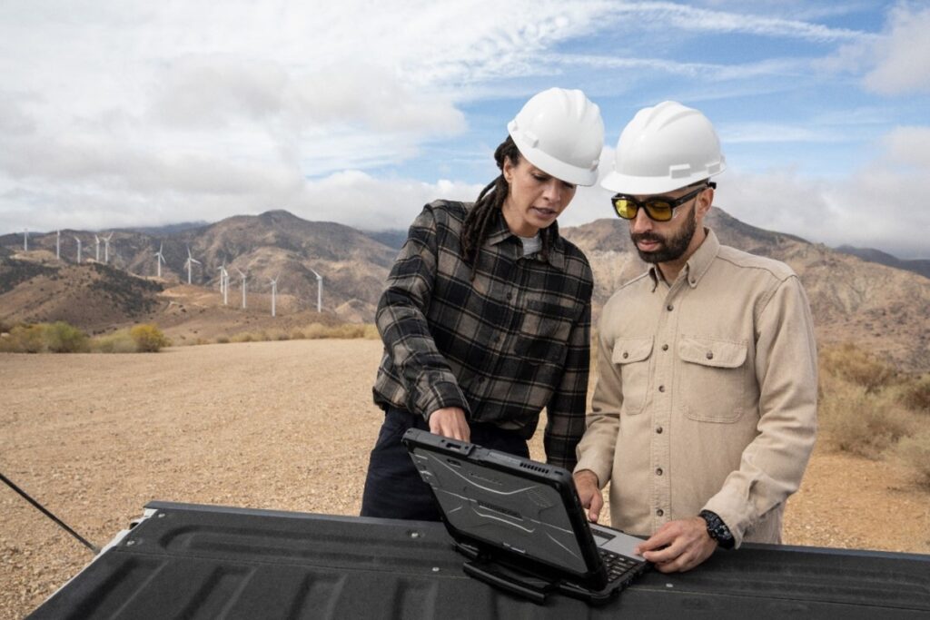 Two people, outside, looking at a laptop that is sitting on an open truck bed.