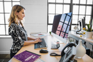 Female office worker standing at desk using desktop computer. Blank screen shown.
