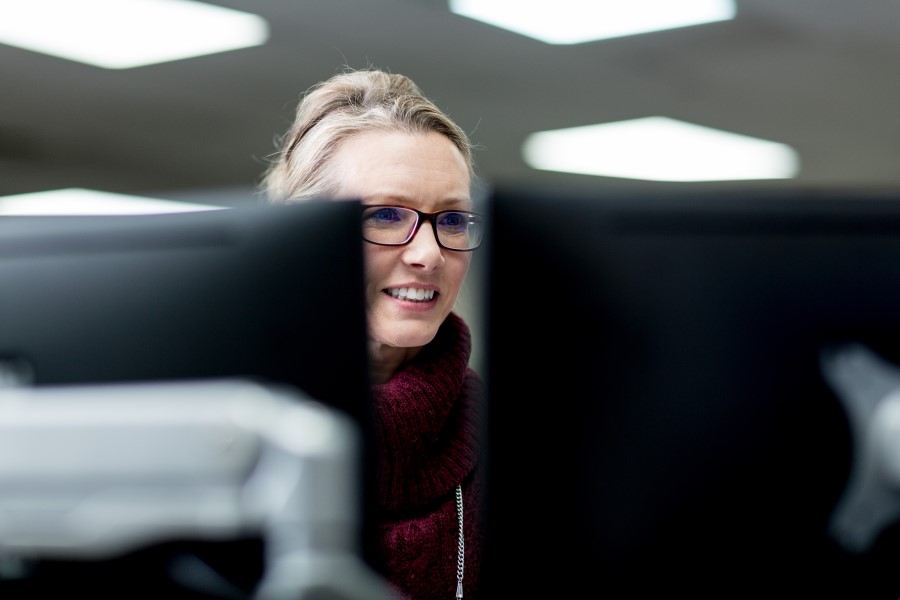 Female worker wearing glasses and looking at one of two desktop monitors