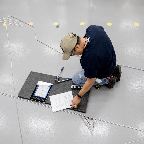 Overhead view of male worker kneeling on manufacturing factory floor and reaching for notes written on paper.