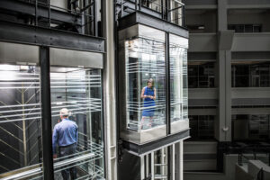 Photo of a business woman and man in separate glass elevators.