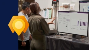 Photograph of two employees looking at a large computer monitor, incorporating the Dynamics 365 Field Service icon