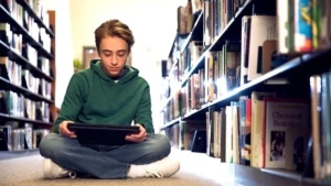 Ein Schüler sitzt auf dem Boden einer Bibliothek und liest ein Buch