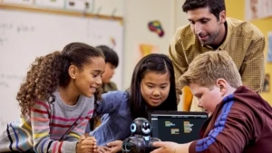 Eine Gruppe von jungen Lernenden beschäftigt sich im Beisein eines Lehrers mit einem Wonder-Workshop-Cue-Roboter und trainiert dabei sozial-emotionale Fähigkeiten.