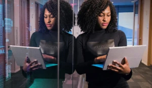 Eine Frau mit einem Laptop in der Hand spiegelt sich in einer Glasscheibe