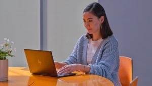 Eine Frau sitzt an einen braunen Holztisch und arbeitet an einem Laptop