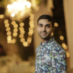 Photo of Danish Jafri, a smiling man with dark hair in a patterned shirt standing in front of fairy lights