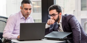Homens em sala de reunião conversando e olhando para computador.